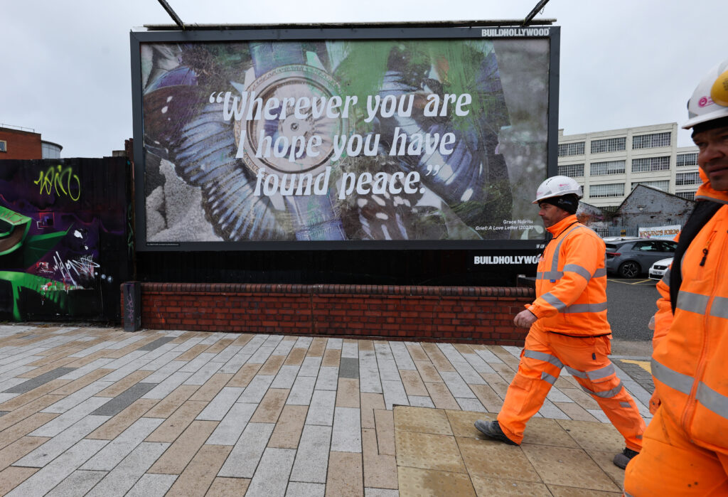 In the image persons are in front of a billboard that has the work of Ndiritu and the sentence: Wherever you are I hope you have found piece.