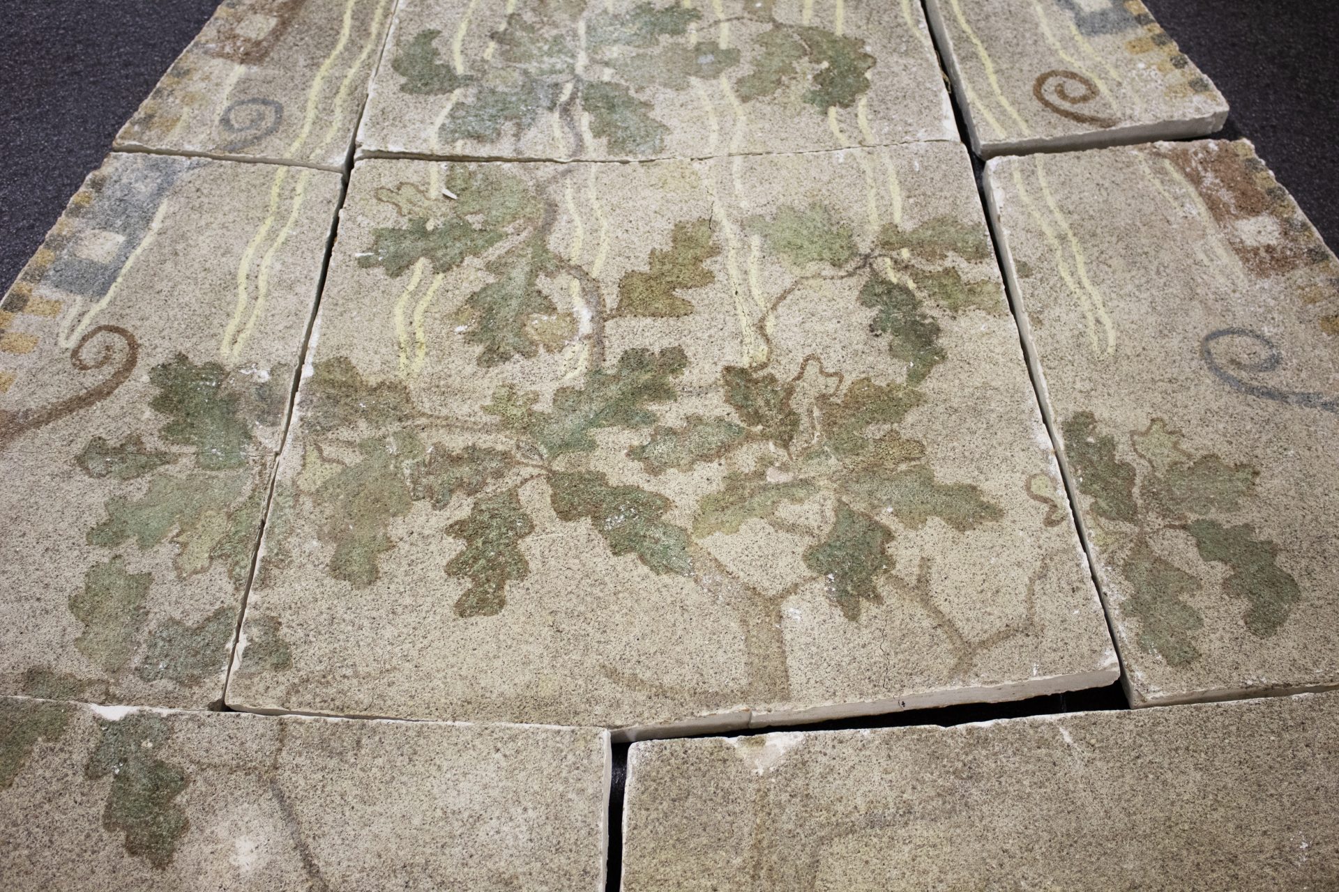 Kulunut fresko, jossa vihreitä tammenlehviä epäsäännöllisillä kivi- tai laastinpaloilla.